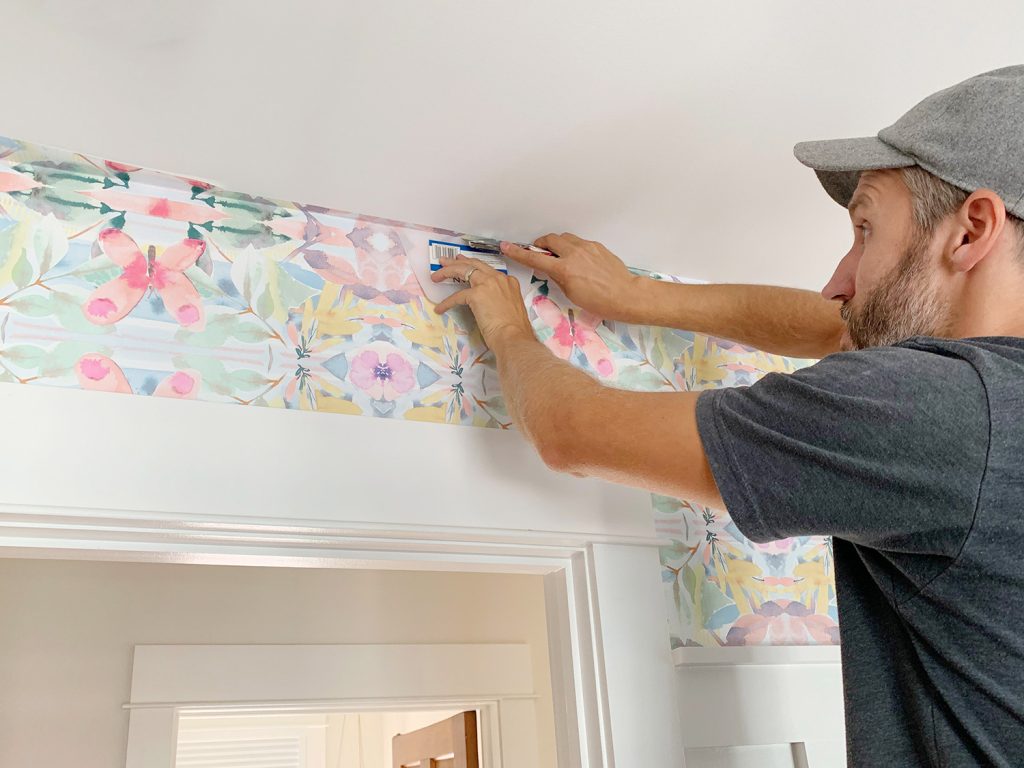 Cutting Excess Peel And Stick Wallpaper Against Ceiling With Knife