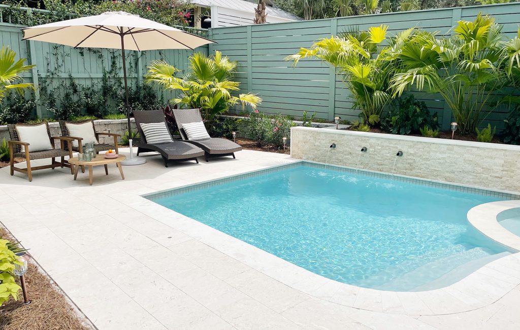 Small freeform pool enclosed by green fences with DiamondBrite Ivory plaster and shellstone travertine