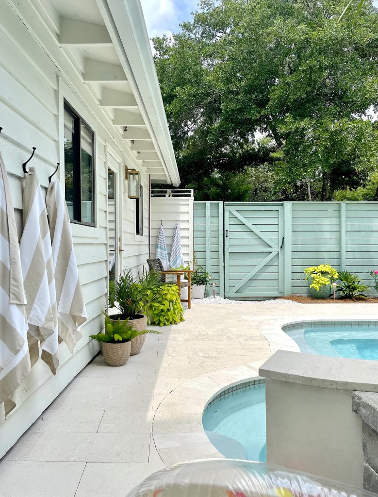 Matching wicker chair sitting on opposite end of pool among potted plants and hook towel storage